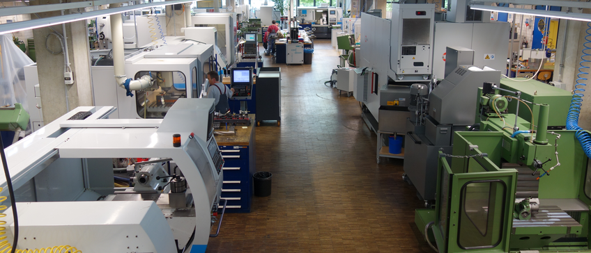 Spacious factory floor of our mechanical workshop featuring modern machinery, including CNC machines and workstations, with workers attending to different manufacturing tasks.