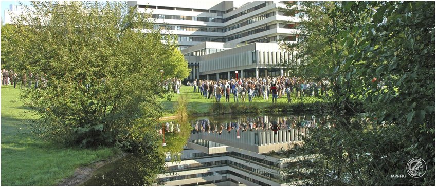 Equal Opportunity A crowd is gathered on a grassy field. Behind them is the multi-story building of the MPI FKF. The building and crowd are clearly reflected in a nearby pond, surrounded by greenery.